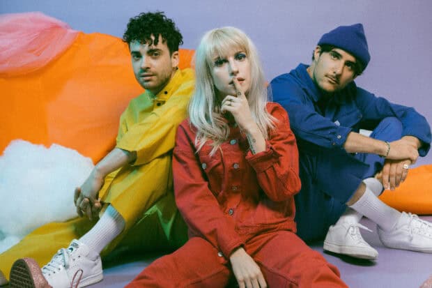 The Paramore band members sit in vibrant clothes with an orange and purple background, HD Desktop Wallpaper