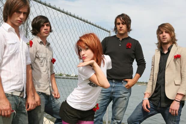 The Paramore band poses by a waterfront fence with red flowers attached to their outfits, 2K Desktop Wallpaper