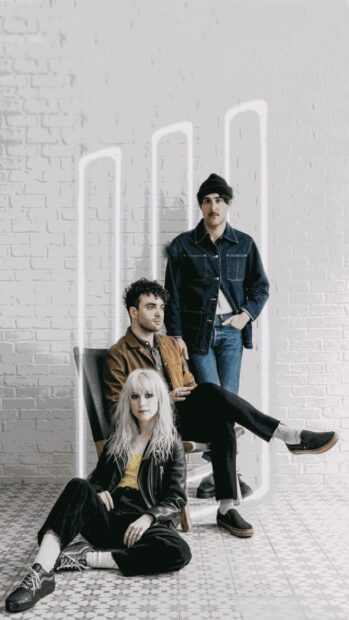 The Paramore band members pose against a white brick wall with neon lights, HD Mobile Wallpaper