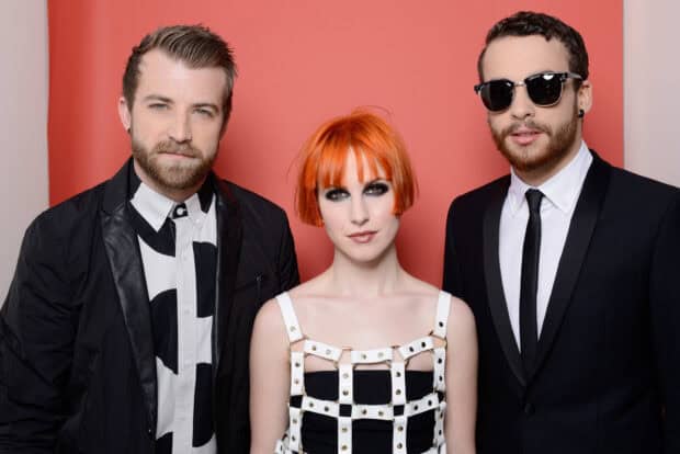 Paramore wallpapers featuring the band members in stylish outfits posing against a red backdrop, HD Desktop Wallpaper