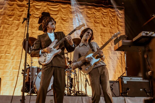 Two members of Parcels band playing electric guitars on stage, 2K Desktop Wallpaper