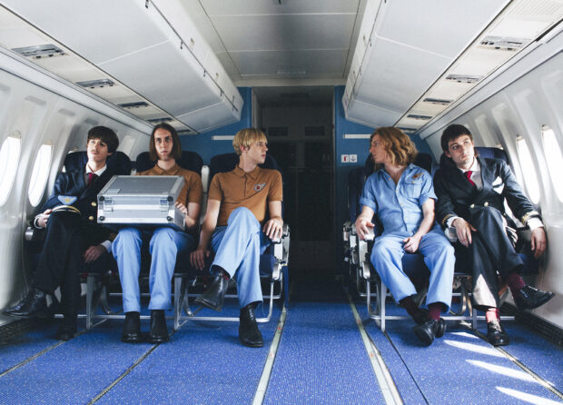 The Parcels band members are seated together inside a plane cabin in casual and pilot style outfits, HD Desktop Wallpaper