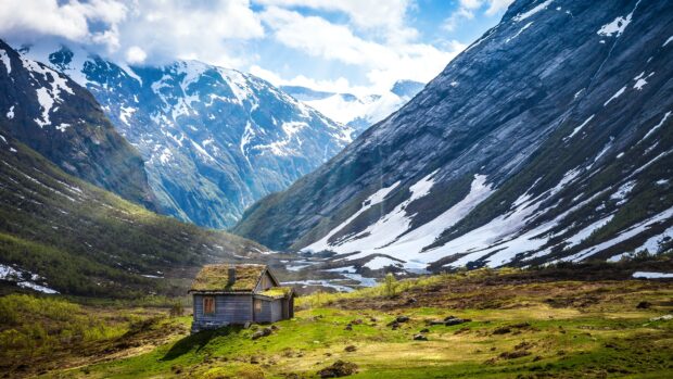 A peaceful cabin sits in a green valley with snowy mountains in Norway, 4K Desktop Wallpaper