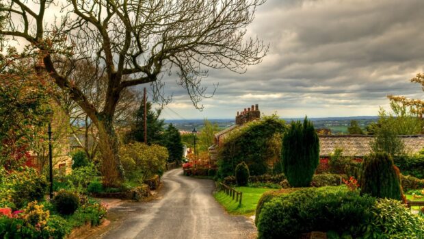 A peaceful village road with lush greenery and old houses under a cloudy sky featuring village wallpapers, HD Desktop Wallpaper