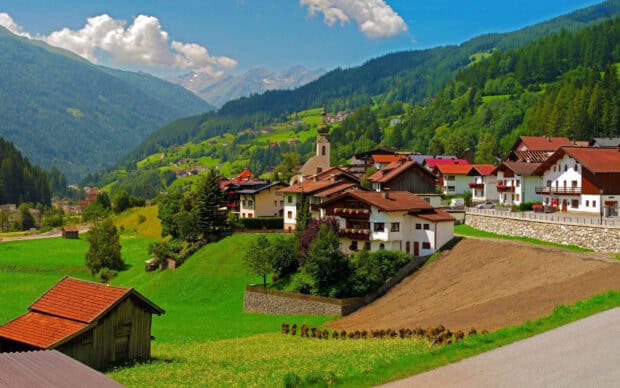 A beautiful village surrounded by green hills and mountains in a bright sunny day featuring village wallpapers, 2K Desktop Wallpaper
