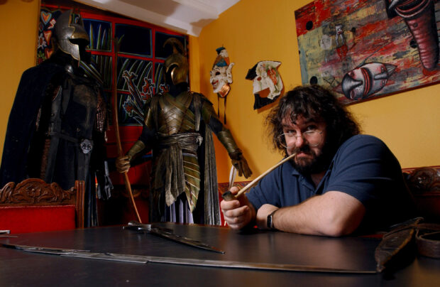 A man posing with medieval armor and masks in a creative room featuring Peter Jackson wallpapers, 2K Desktop Wallpaper