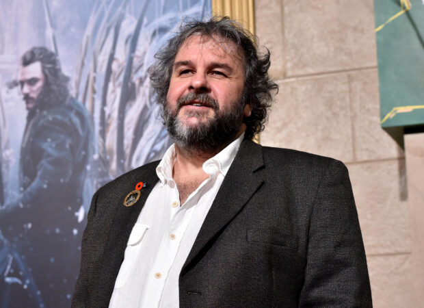 Peter Jackson stands outdoors near a movie poster in a dark suit and white shirt, 2K Desktop Wallpaper