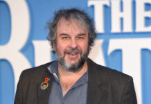 Peter Jackson smiles wearing a lapel pin on a blue background, 2K Desktop Wallpaper