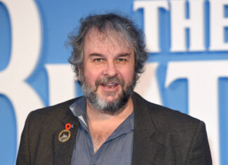 Peter Jackson smiles wearing a lapel pin on a blue background, 2K Desktop Wallpaper