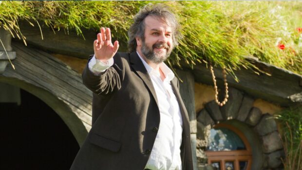 Peter Jackson smiles and waves in front of a rustic grass roof house, HD Desktop Wallpaper