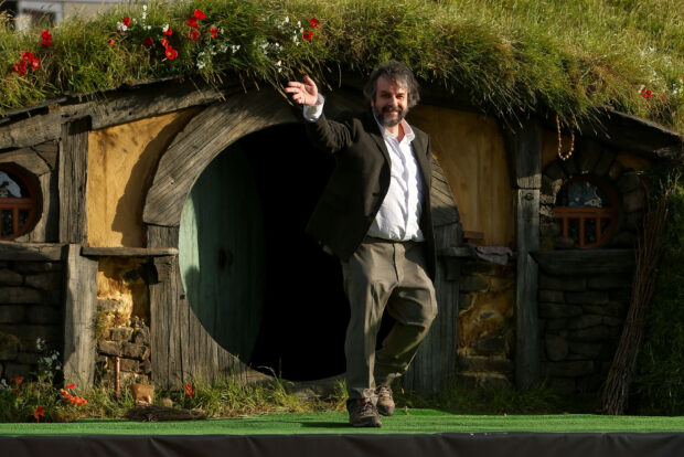 Peter Jackson stands outside a rustic hobbit house with a circular door and greenery, 2K Desktop Wallpaper