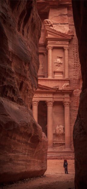 A person stands in front of the ancient facade carved in the rock of Petra Jordan, 2K Mobile Wallpaper