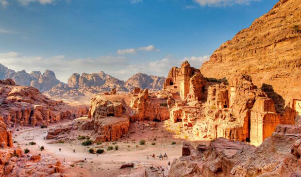 A panoramic view of Petra Jordan reveals ancient rock structures under a clear blue sky, HD Desktop Wallpaper