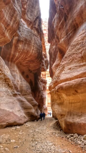 A group of people walking through a narrow canyon in Petra Jordan with rocky cliffs on both sides, HD Mobile Wallpaper