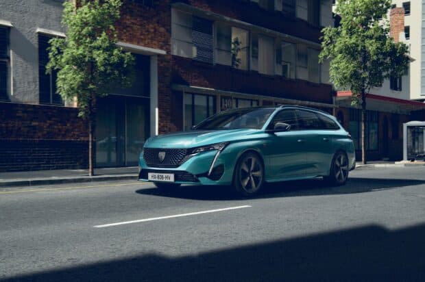 A sleek turquoise Peugeot 308 driving on a city street with buildings and trees in the background, 2K Desktop Wallpaper