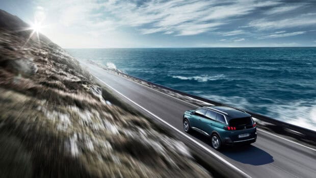 A Peugeot 5008 drives along a coastal highway with the ocean in the background, 2K Desktop Wallpaper