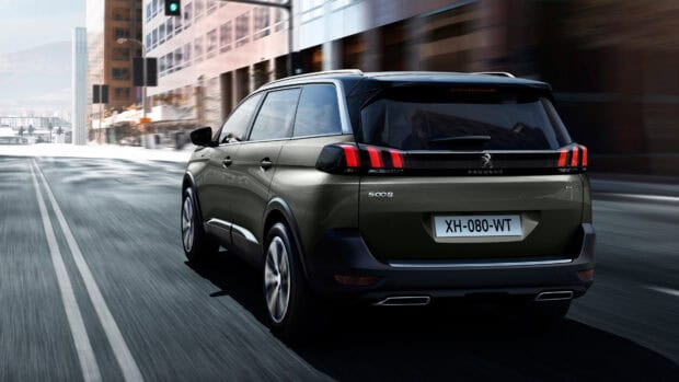 A Peugeot 5008 drives fast through a city road with modern buildings on the side, 4K Desktop Wallpaper