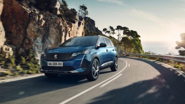 A blue Peugeot 5008 driving along a winding coastal road with rocky cliffs and trees, 4K Desktop Wallpaper