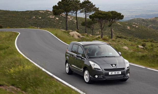 A Peugeot 5008 is driving along a curved mountain road with green trees and hills around, 2K Desktop Wallpaper