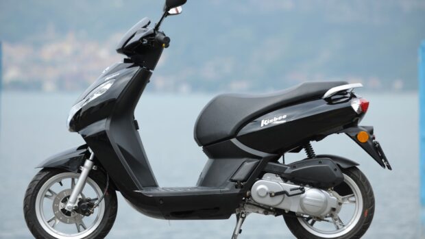 A black Peugeot Kisbee scooter is parked near water with a blurred background, HD Desktop Wallpaper