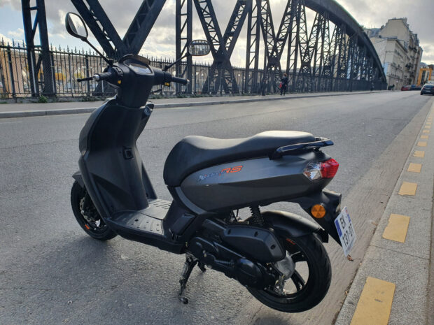 A Peugeot Kisbee scooter is parked near a steel bridge in the city, HD Desktop Wallpaper