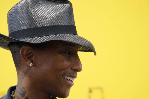 Pharrell Williams wears a textured hat and smiles against a yellow background, 2K Desktop Wallpaper