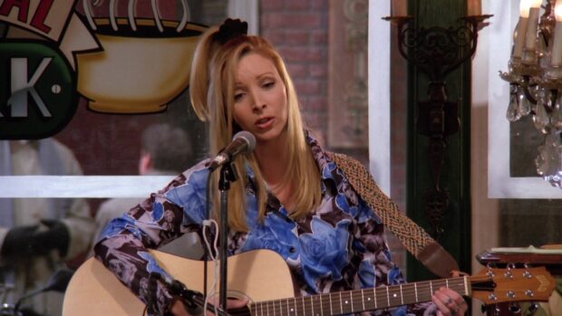 Phoebe Buffay is singing while playing an acoustic guitar on stage, HD Desktop Wallpaper