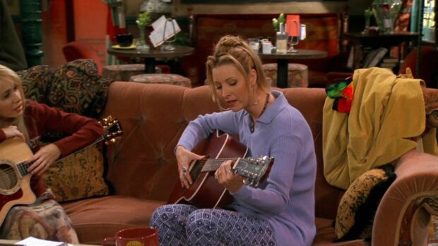 Phoebe Buffay is playing a guitar while sitting on a couch in a cozy cafe setting, HD Desktop Wallpaper