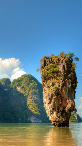 A tall limestone rock formation covered with greenery rises from calm waters near Phuket, 4K Phone Wallpaper