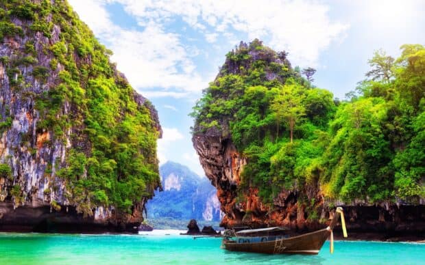 A traditional boat floats near green limestone cliffs in turquoise water of Phuket HD Desktop Wallpaper