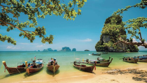 Traditional wooden boats rest near the sandy shore in Phuket with clear blue water and sky, 4K Desktop Wallpaper