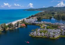 A scenic coastal view in Phuket showcases the turquoise sea and lush greenery with buildings, HD Desktop Wallpaper