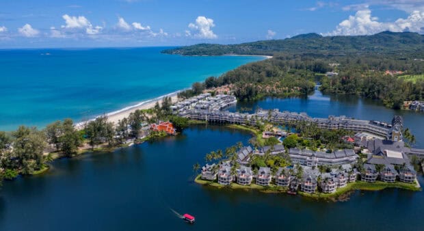 A scenic coastal view in Phuket showcases the turquoise sea and lush greenery with buildings, HD Desktop Wallpaper