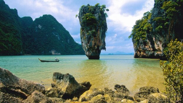 A small boat sails near limestone cliffs in Phuket with calm water and blue sky, HD Desktop Wallpaper
