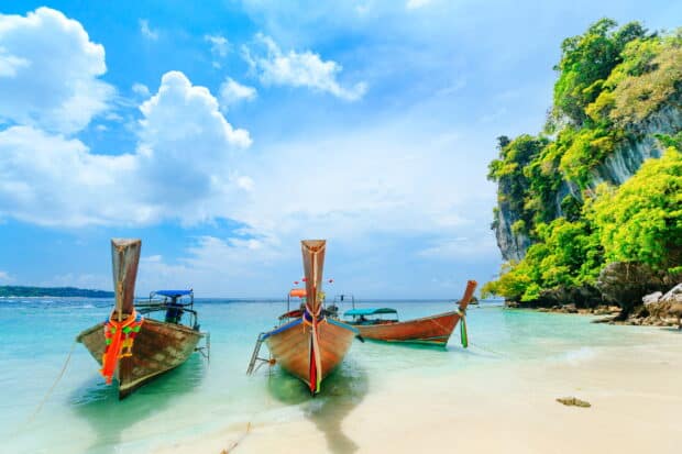 Three long tail boats rest on clear turquoise water near lush cliffs in Phuket, HD Desktop Wallpaper