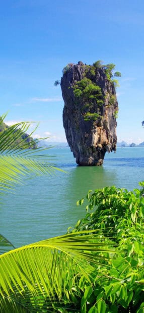 A tall rock formation surrounded by sea and greenery in Phuket, HD Phone Wallpaper