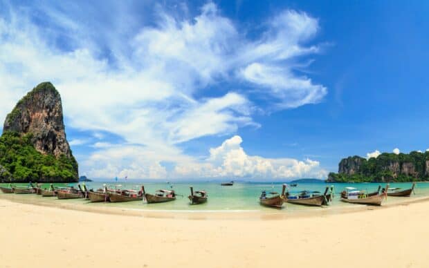 Traditional longtail boats line the shore under blue skies in Phuket for Phuket Wallpapers, 2K Desktop Wallpaper
