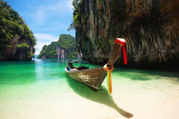 A traditional wooden boat floats in clear water near rocky cliffs in Phuket, HD Desktop Wallpaper