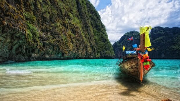 A wooden boat rests on the clear turquoise sea near Phuket cliffs, HD Desktop Wallpaper