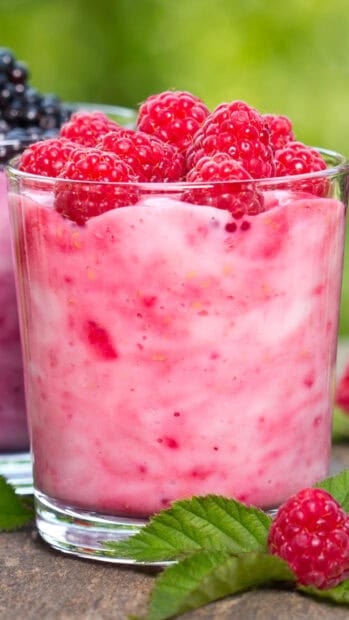 A glass of pink berry milkshake topped with fresh raspberries and green leaves outside, 2K Mobile Wallpaper