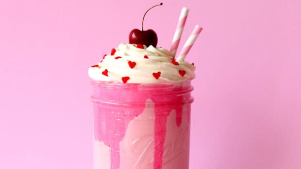 A pink milkshake topped with whipped cream, red heart sprinkles, and a cherry with two striped straws, 2K Desktop Wallpaper