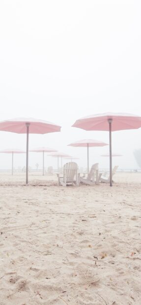 Several pink umbrellas stand on the sandy beach with wooden chairs underneath, 2K Phone Wallpaper