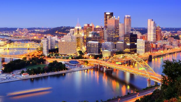 The Pittsburgh skyline features illuminated buildings and bridges along the river during sunset, 2K Desktop Wallpaper