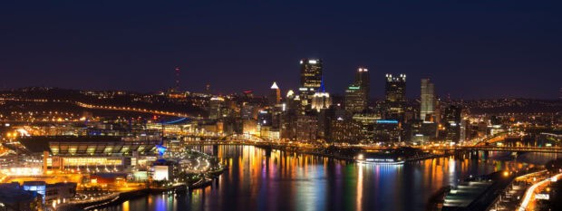 The Pittsburgh skyline features illuminated buildings and reflections in the river at night, 4K Desktop Wallpaper