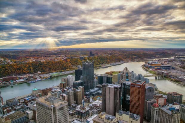 The Pittsburgh skyline shows buildings along the river with sun rays breaking through clouds, HD Desktop Wallpaper