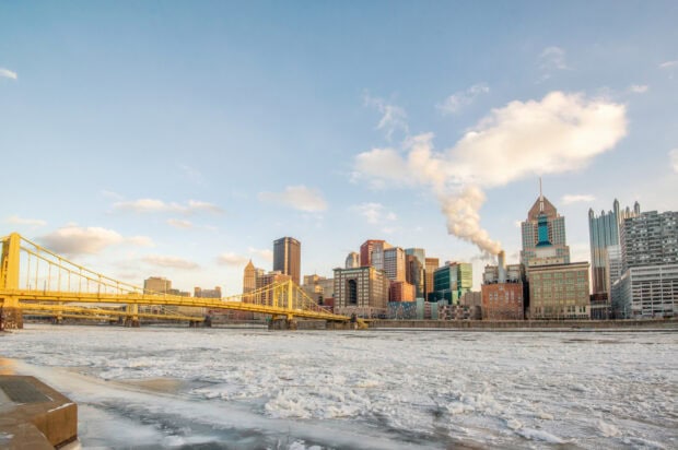 The Pittsburgh skyline shows frozen river and buildings with a yellow bridge under a partly cloudy sky, HD Desktop Wallpaper
