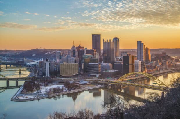 The Pittsburgh skyline features tall buildings and bridges over calm rivers under a golden sunset, HD Desktop Wallpaper