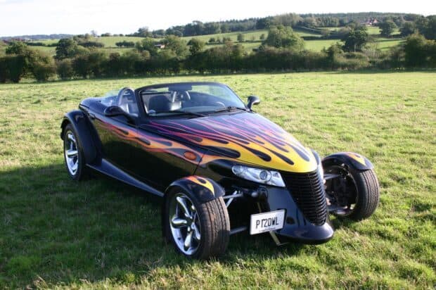 A black Plymouth Prowler with yellow and orange flames parked on a green grassy field, HD Desktop Wallpaper