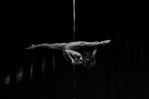 A woman demonstrates strength and flexibility during a pole dance performance, HD Desktop Wallpaper