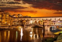 The Ponte Vecchio bridge glows warmly over the Arno River at sunset with vibrant skies, 4K Desktop Wallpaper